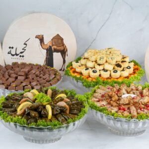 A beautifully arranged assortment of chocolates, stuffed pastries, and grape leaves on glass platters with decorative green lettuce, set against a backdrop featuring "Kahelah" branding with a camel illustration.